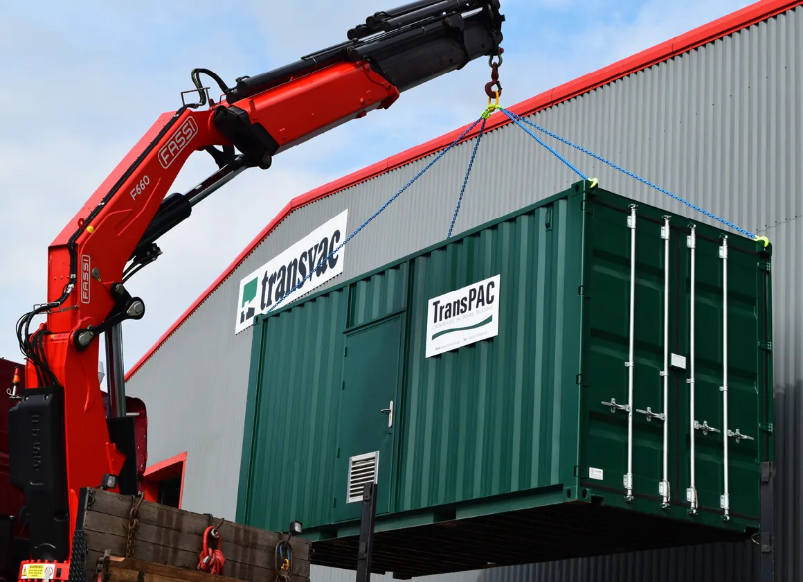 A green container branded “TransPAC” being lifted by a red crane outside the Transvac building, showcasing its mobility and ease of deployment.