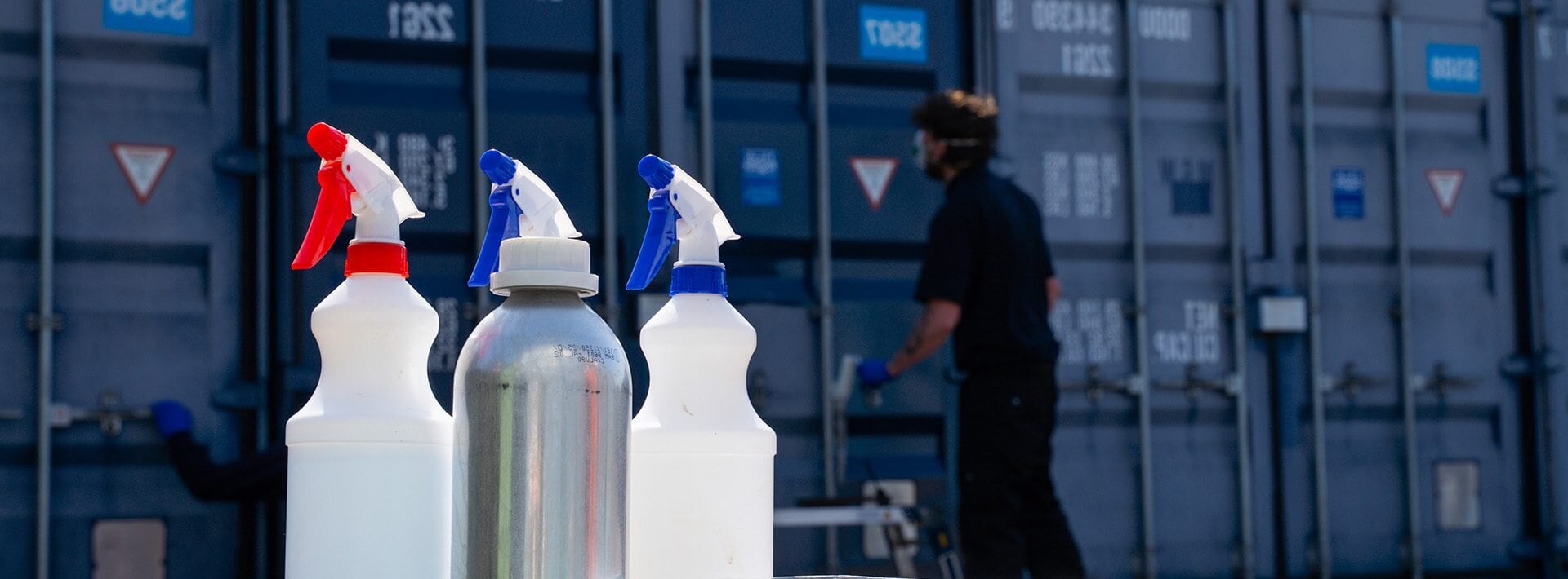 Close-up of cleaning bottles, rollers, and cloths in front of shipping containers being restored with ClearRestore®, a specialist container colour revival treatment.