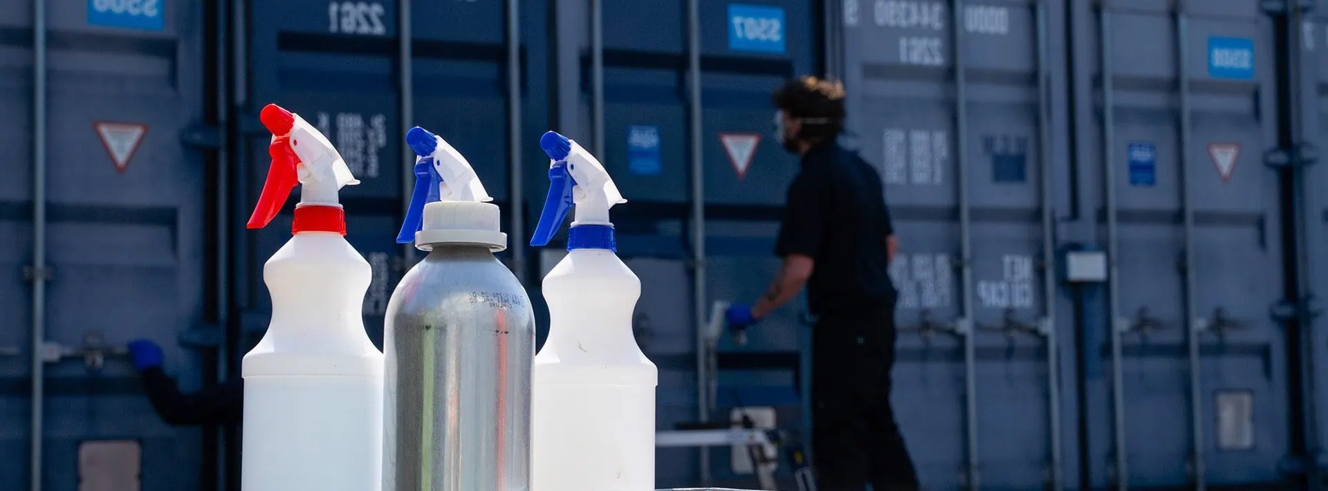 Close-up of cleaning bottles, rollers, and cloths in front of shipping containers being restored with ClearRestore®, a specialist container colour revival treatment.