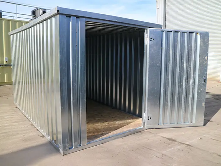 A galvanised flat pack metal storage unit with its door open, showing the corrugated steel walls and wooden flooring inside.