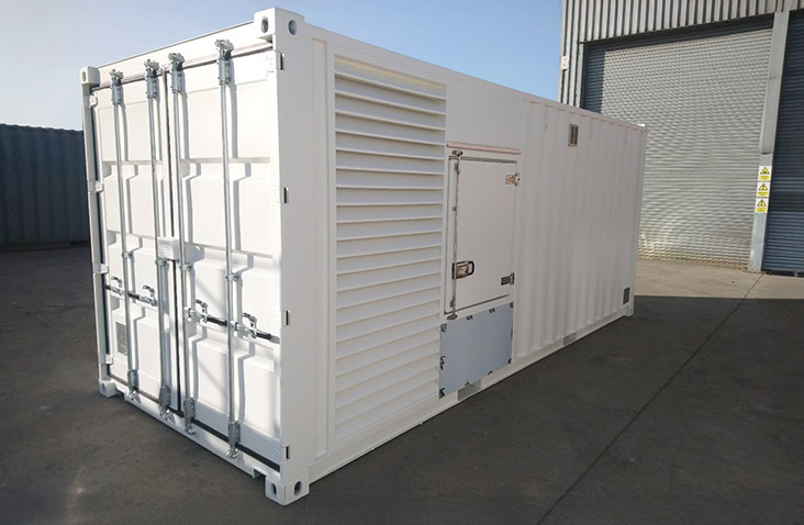 Interior corridor of a container unit with multiple roller shutter doors on both sides, leading to a bright yellow balustrade at the far end.