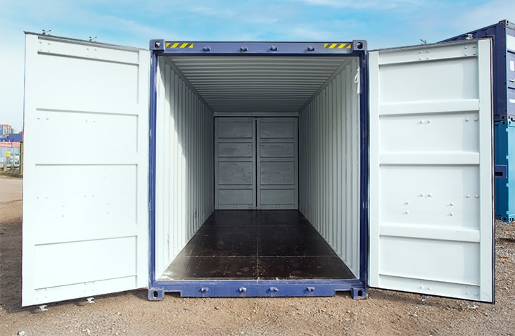 Front view of a blue 20ft high cube shipping container with both sets of doors open, revealing a clean, empty interior and dark plywood flooring on a gravel yard.