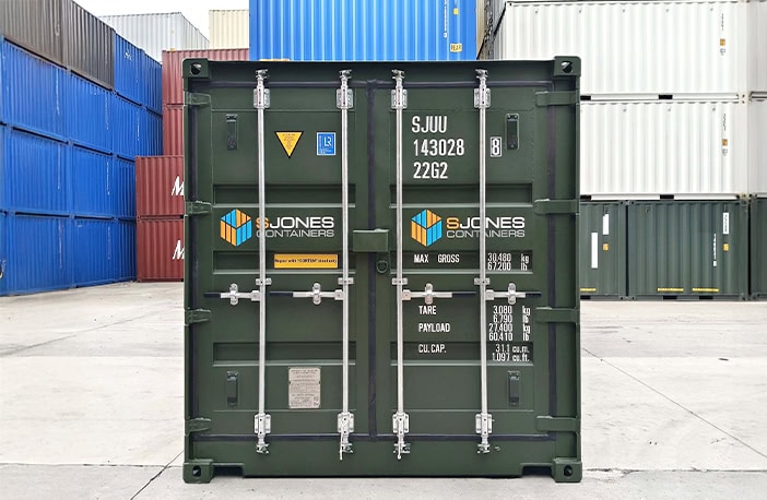 End view of a green 20ft side opening shipping container showing closed cargo doors with S Jones Containers branding, positioned in a container yard with stacked containers in the background