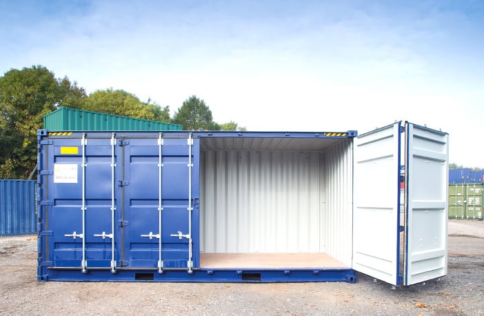     Blue 40ft high cube side opening shipping container with one side door open, revealing the light interior and wooden flooring, positioned in a storage yard with other containers and trees in the background. 