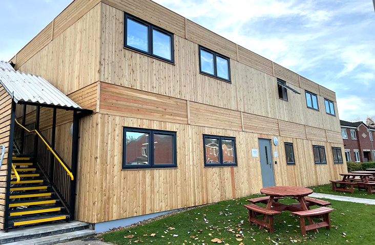 Timber-clad modular welfare facility with multiple windows and external staircase, providing site accommodation and welfare space for staff use.