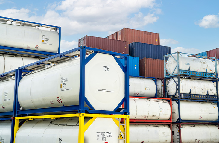 Stacks of tank containers and standard shipping containers stored at a depot, highlighting mixed container types used for liquid transport and general freight storage.