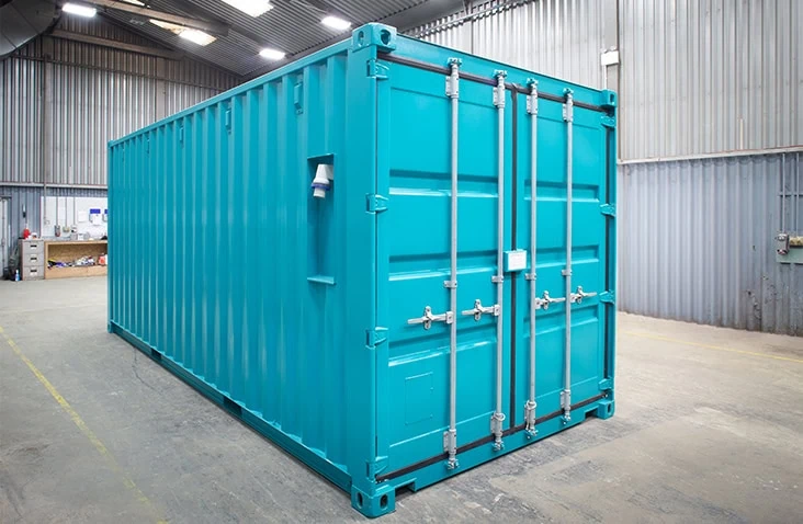 Exterior of a bright turquoise laboratory container unit positioned inside a workshop, featuring double cargo doors and secure lock fittings.