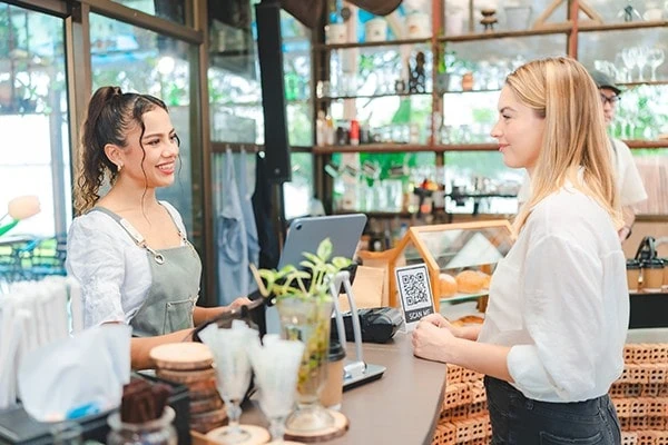 Customer paying at a café counter while a barista smiles behind the till, representing hospitality, retail service and customer experience. 