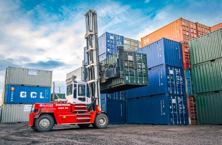 Container handler stacking a green shipping container among rows of containers at the S Jones Aldridge depot, showing active container handling and logistics operations. 