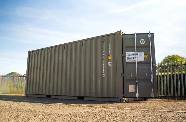 20ft green steel shipping container positioned on a yard beside metal fencing, branded with the S Jones Containers hire label.