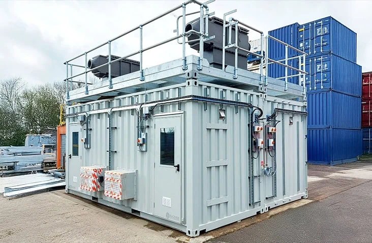 Battery destruction testing unit built from a converted shipping container, showing a reinforced container with rooftop exhaust systems, safety railings, electrical control panels and ventilation equipment for controlled battery testing and failure analysis.