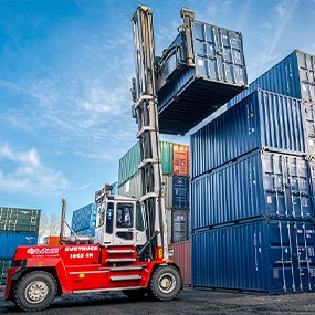 Container handler lifting and stacking blue shipping containers at a secure container depot, showing large-scale container handling and logistics operations for hire and sale.