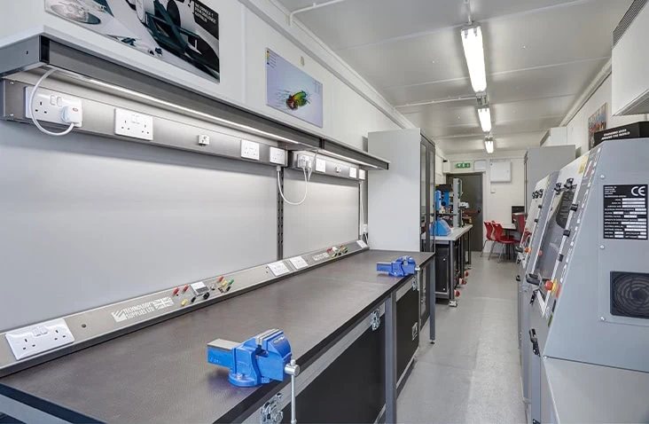 Interior of a containerised STEM workshop featuring fixed workbenches, electrical sockets, vices and industrial machinery, designed as a practical learning space for students inside a converted shipping container.