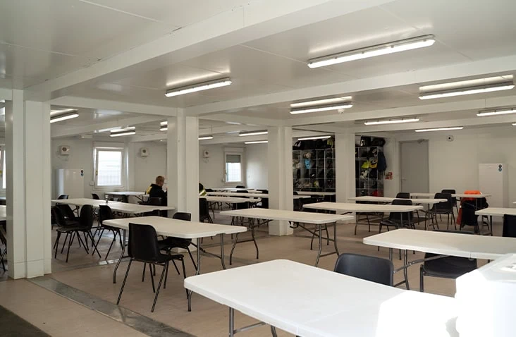 Interior of a large modular canteen building with rows of tables and chairs, bright LED lighting and open layout, designed for workforce welfare on construction and infrastructure sites. 