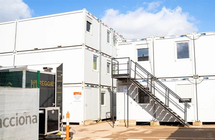 Three-storey modular welfare and office complex with external staircase, stacked modular units and windows, providing scalable site accommodation for construction projects.