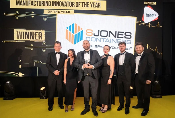 S Jones Containers team celebrating on stage at the Innovation Awards 2025 after winning an award for manufacturing innovation. Team members are pictured in formal evening wear holding the trophy in front of a large screen displaying the S Jones Containers logo and winner announcement, recognising the company's achievements in engineering, innovation, and shipping container conversions.