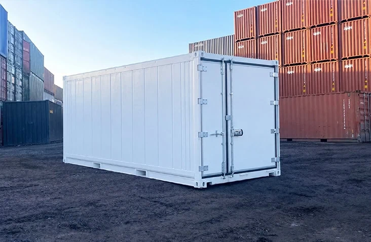 White 20ft refrigerated shipping container (reefer) shown in a container depot, with stacked shipping containers in the background. Designed for temperature-controlled storage and transport, the refrigerated shipping container operates between -25°C and +25°C and is available to hire from S Jones Containers with a minimum hire period of 90 days.