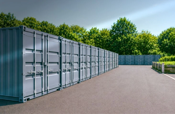 Modern containerised self-storage facility featuring rows of clean grey shipping containers arranged around a wide tarmac access area. The secure drive-up storage units provide convenient vehicle access for loading and unloading, demonstrating how shipping containers can create a professional, space-efficient external self-storage site for domestic and business customers.
