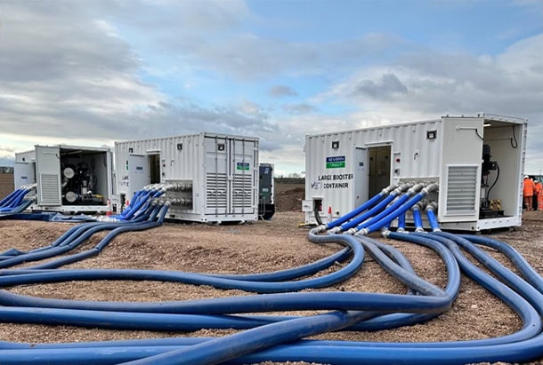 Three 20ft shipping containers converted into bespoke containerised pump houses by S Jones Conversions division for Grundfos. Installed at an outdoor site, the white steel enclosures feature ventilation grilles, access doors and integrated pumping equipment, with multiple large blue flexible hoses connected to the units and extending across the ground. These specialist container conversions provide practical, purpose-built enclosures for industrial water pumping and treatment applications.